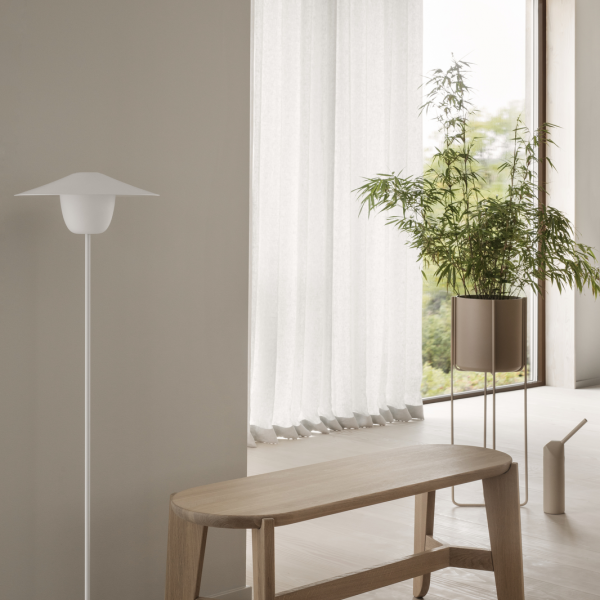 Modern living room with a white floor lamp, bamboo plant, and light curtains.