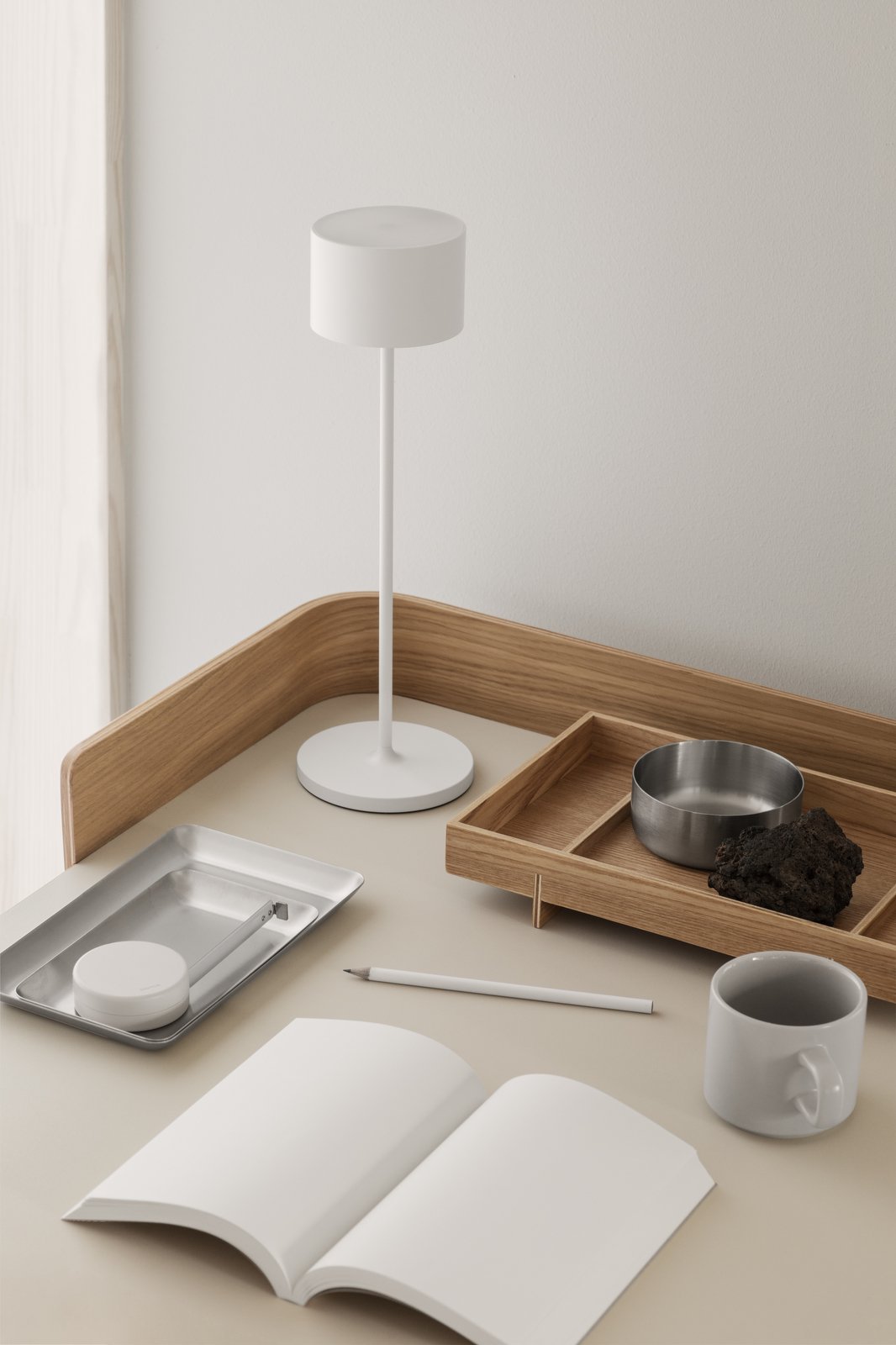 Minimalistischer Schreibtisch mit einer Lampe, Tabletts, einer Tasse und einem dekorativen Stein.
