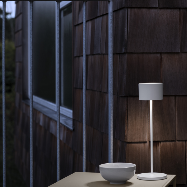 Moderne Tischlampe, die eine minimalistische Außeneinstellung mit Holzverkleidung und einer weißen Schüssel beleuchtet.