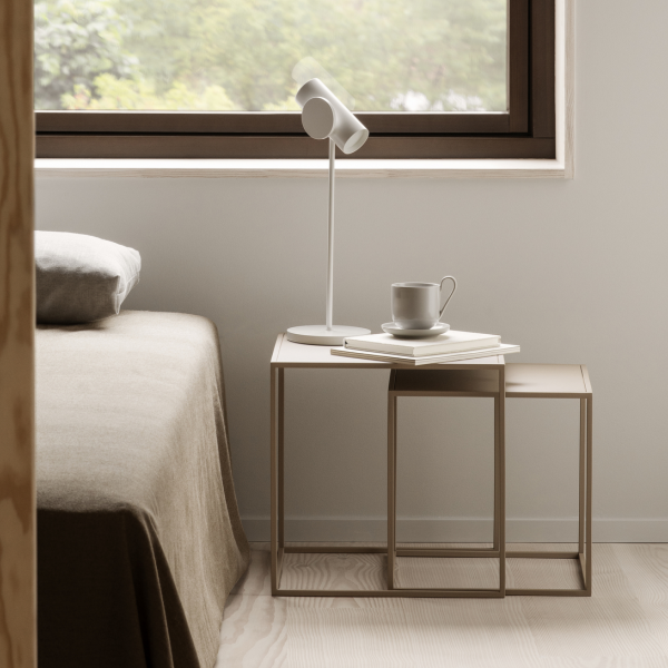 Moderner Schlafzimmer-Szene mit einem minimalistischen Nachttisch, einer Lampe und einer Kaffeetasse neben einem Fenster.