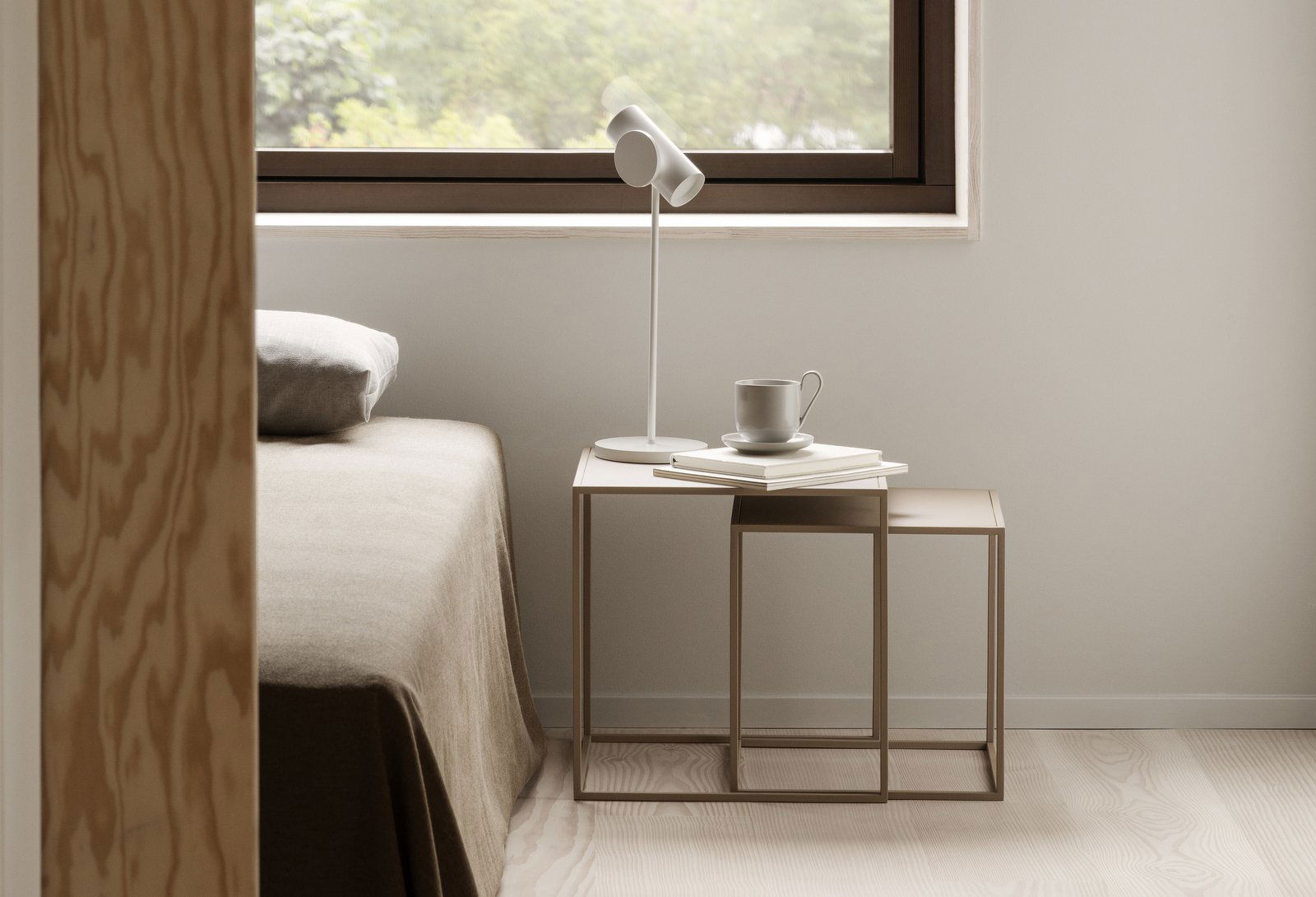 Moderner Schlafzimmer-Szene mit einem minimalistischen Nachttisch, einer Lampe und einer Kaffeetasse neben einem Fenster.