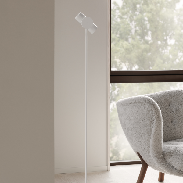 Modern white floor lamp beside a cozy gray armchair in a bright, airy room.