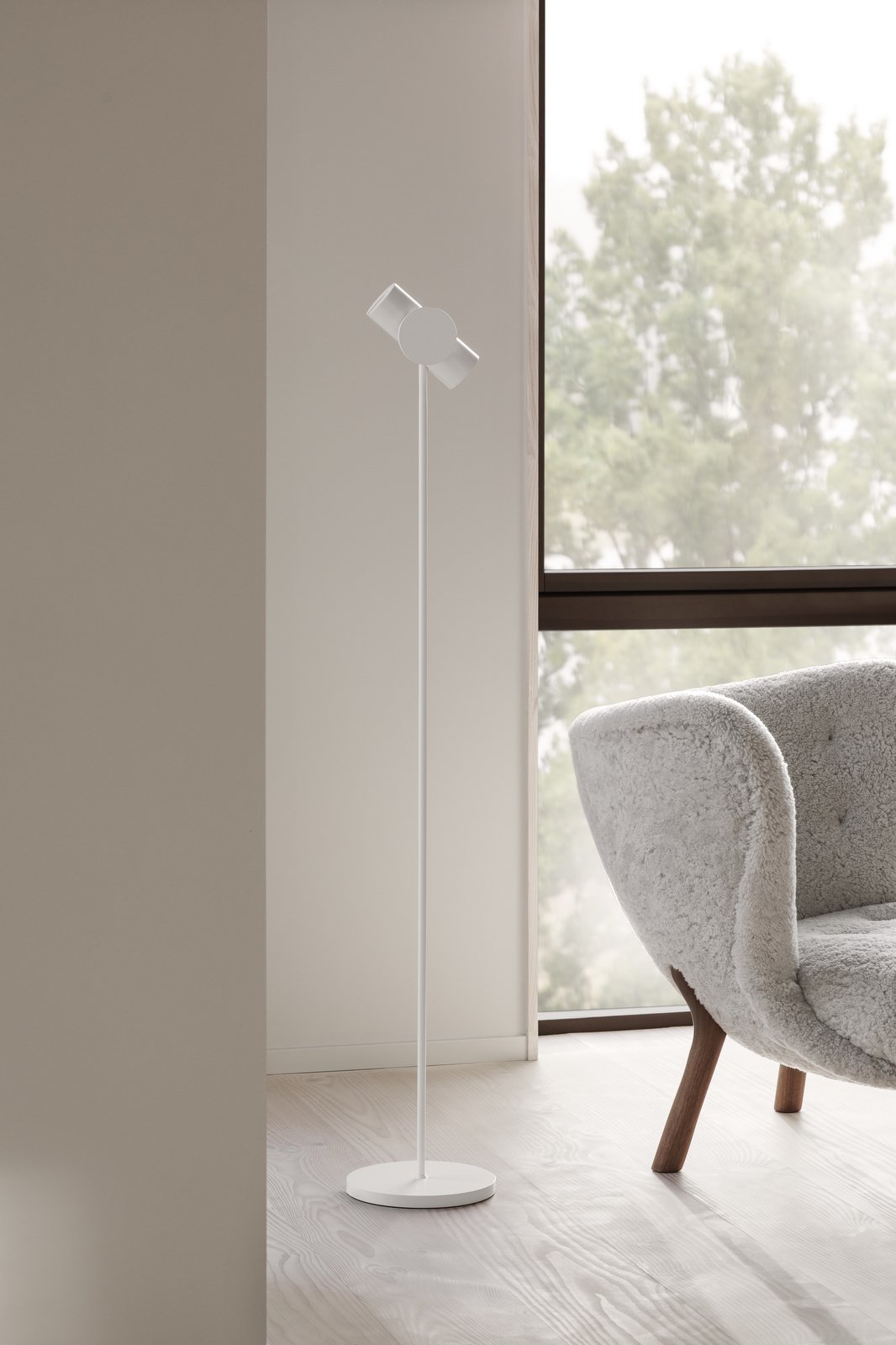 Modern white floor lamp beside a cozy gray armchair in a bright, airy room.