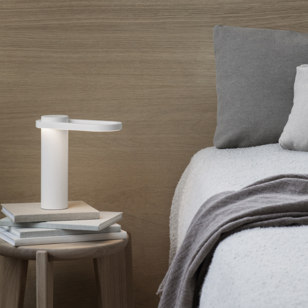 Moderne Nachttischlampe auf einem minimalistischen Nachttisch mit gemütlicher Bettwäsche und strukturierten Kissen.