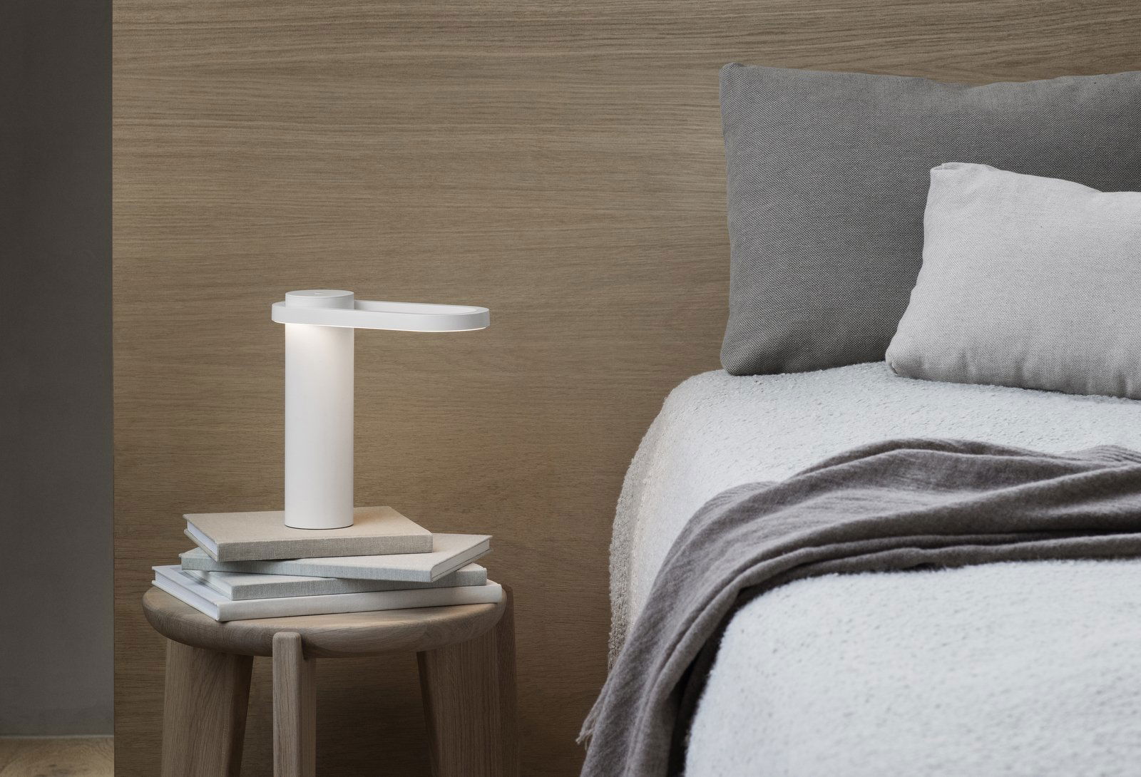 Moderne Nachttischlampe auf einem minimalistischen Nachttisch mit gemütlicher Bettwäsche und strukturierten Kissen.