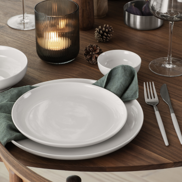 Elegant dinner table setting with white plates, cutlery, and a candle in a glass holder.