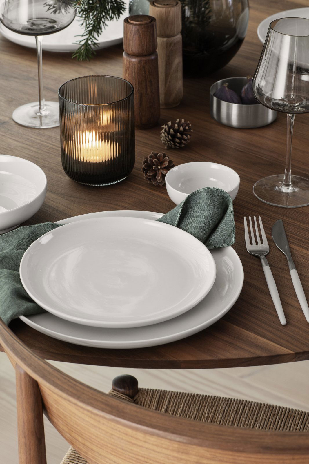 Elegant dinner table setting with white plates, cutlery, and a candle in a glass holder.