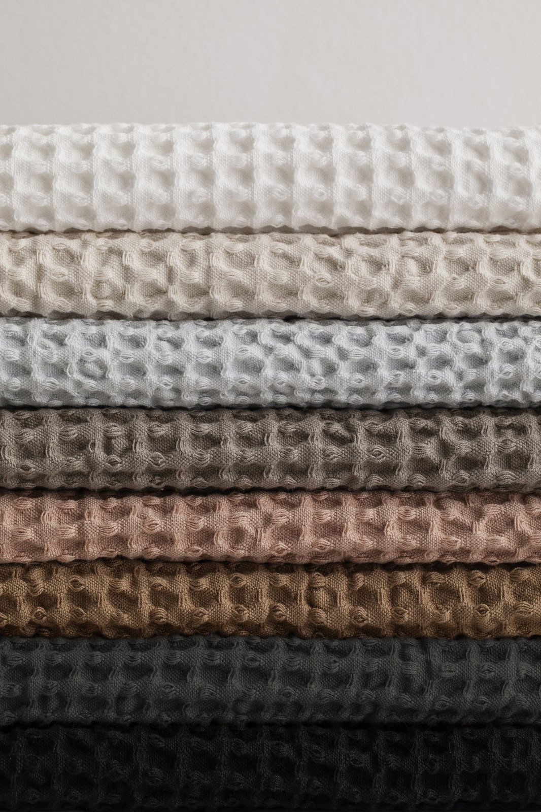 Textured fabric swatches in a gradient of neutral colors stacked neatly on top of each other.