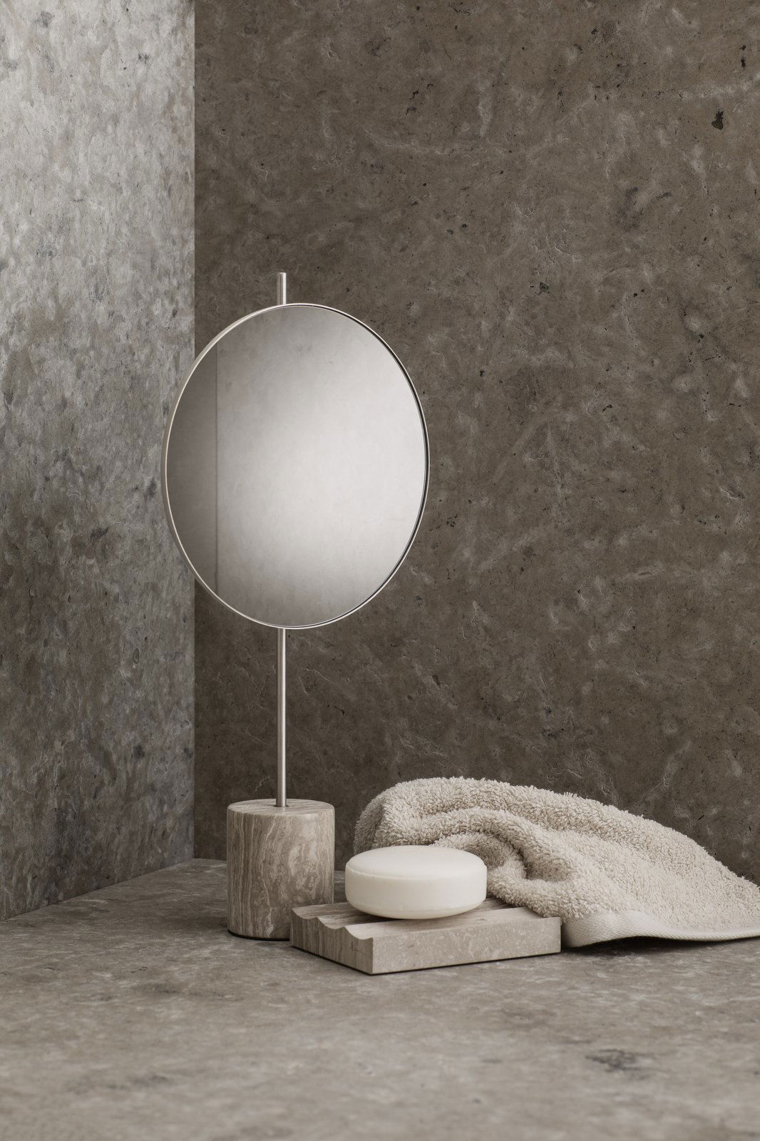 Stylish round mirror on a modern stone countertop with soft towel and soap.