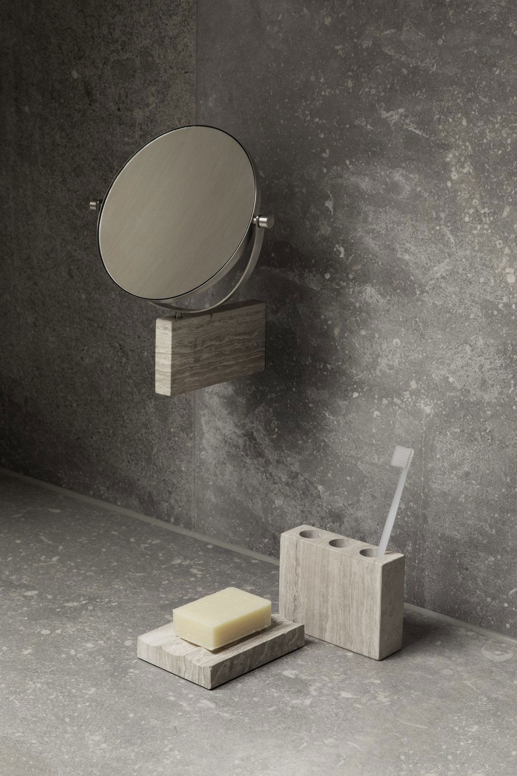 Minimalist bathroom setup with a circular mirror, soap, and toothbrush holder on stone surfaces.