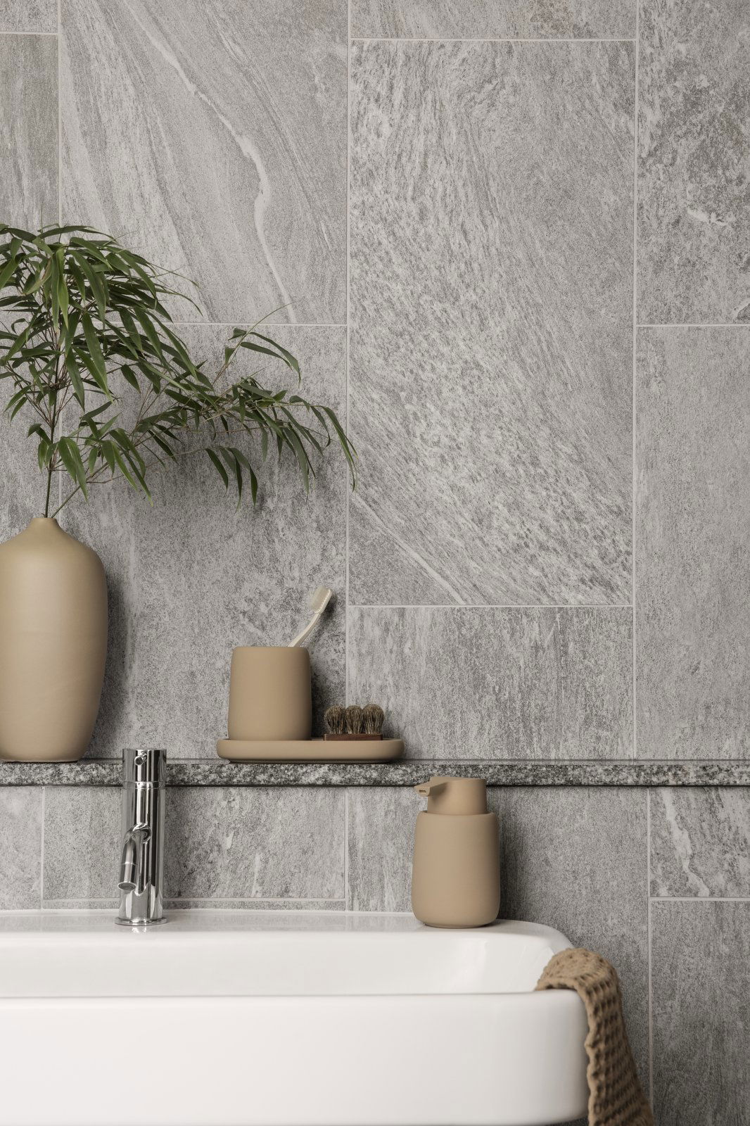 Modern bathroom decor featuring gray stone tiles, earthy vases, and a sleek faucet.