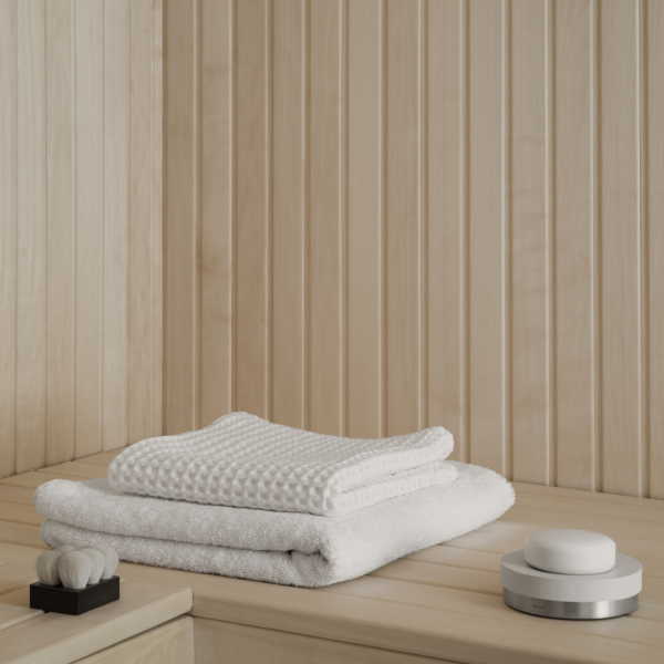 Two neatly stacked white towels on a wooden shelf in a serene, minimalist spa setting.