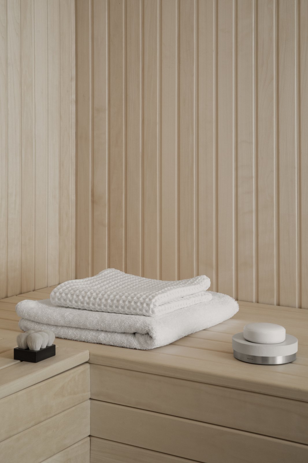 Two neatly stacked white towels on a wooden shelf in a serene, minimalist spa setting.
