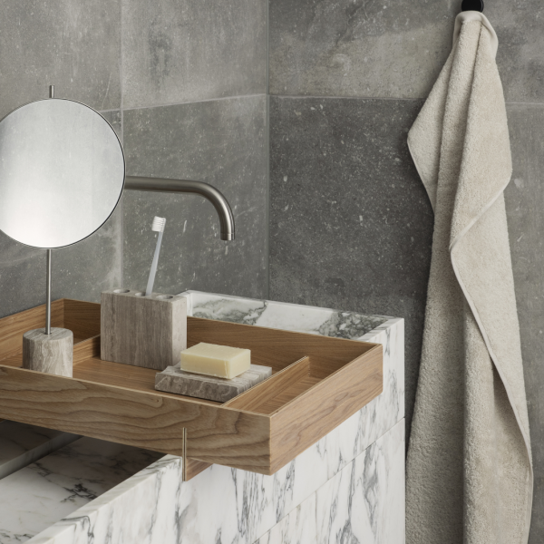 Elegant bathroom countertop with marble, wooden tray, mirror, and soft towel.