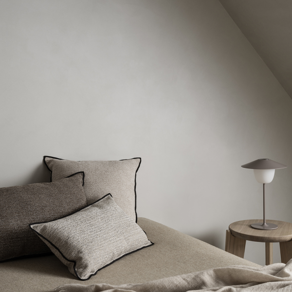 Gemütliche Schlafzimmer-Ecke mit strukturierten Kissen und einer modernen Lampe auf einem Holztisch.
