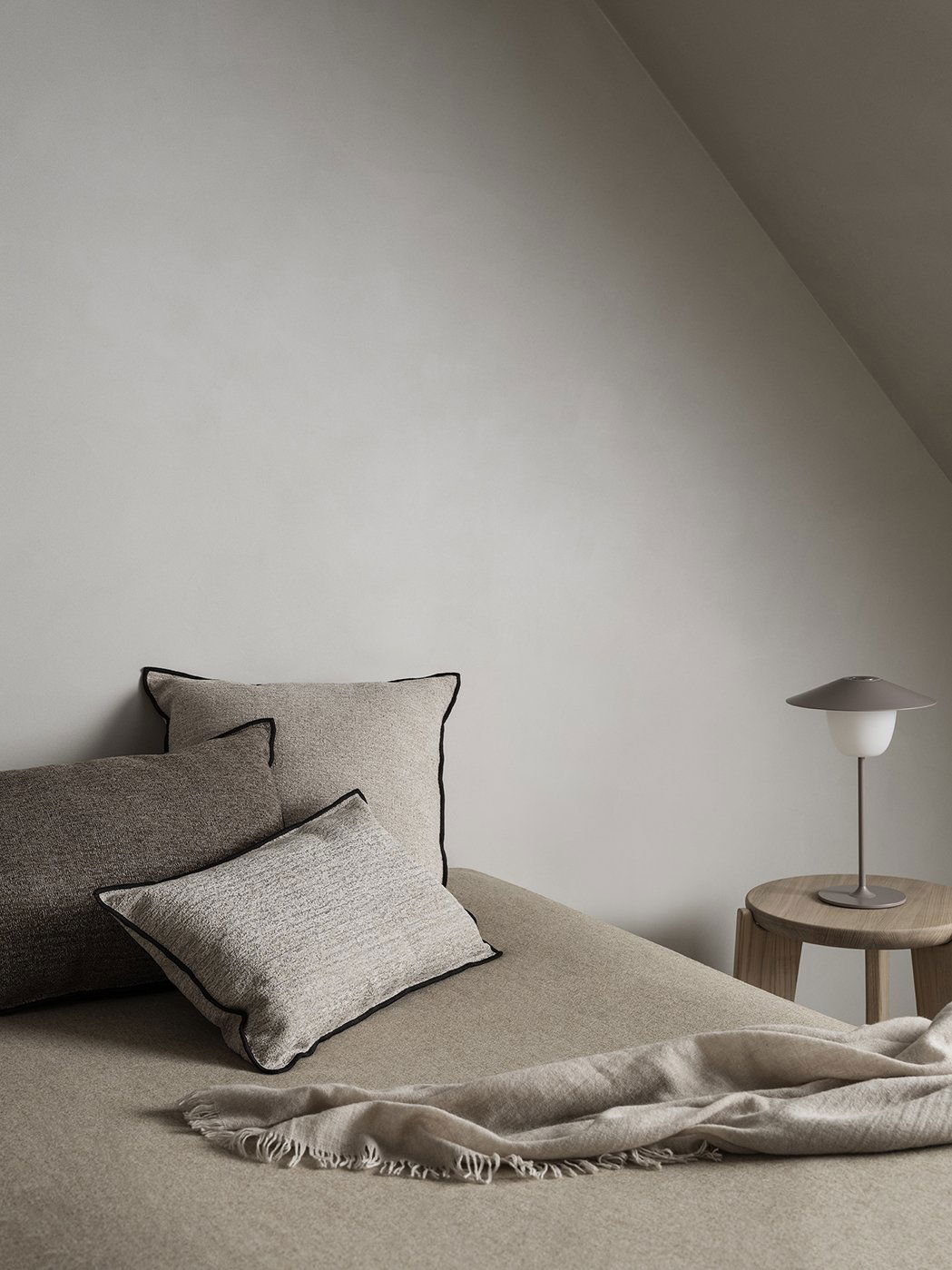 Gemütliche Schlafzimmer-Ecke mit strukturierten Kissen und einer modernen Lampe auf einem Holztisch.