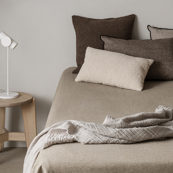 Gemütliche Schlafzimmerdekoration mit neutralen Farben, strukturierten Kissen und weichen Decken auf einem Bett.