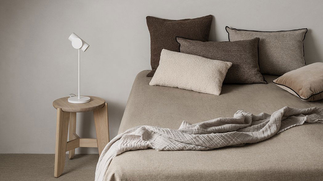 Gemütliche Schlafzimmerdekoration mit neutralen Farben, strukturierten Kissen und weichen Decken auf einem Bett.