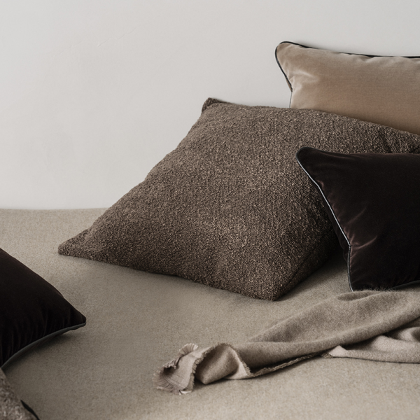 Gemütliche Bett-Szene mit strukturierten Kissen und einer weichen Decke in neutralen Farbtönen.