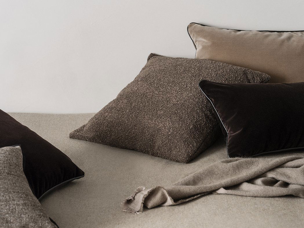 Gemütliche Bett-Szene mit strukturierten Kissen und einer weichen Decke in neutralen Farbtönen.