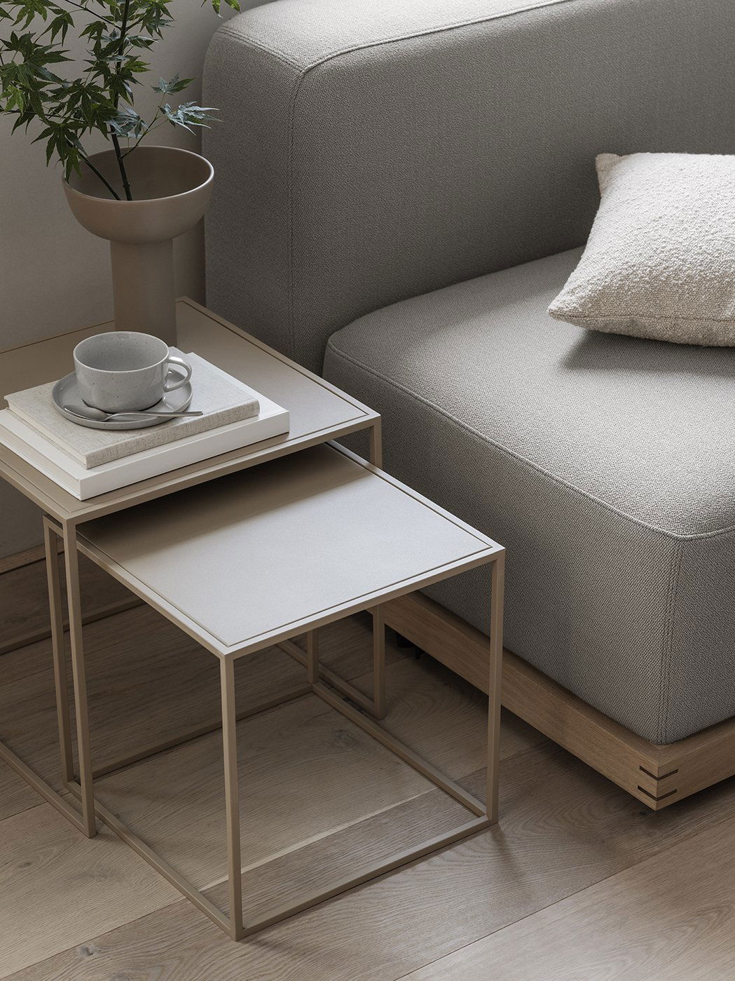 Moderne Wohnzimmergestaltung mit einem grauen Sofa, Beistelltischen und einer gemütlichen Tasse Kaffee.