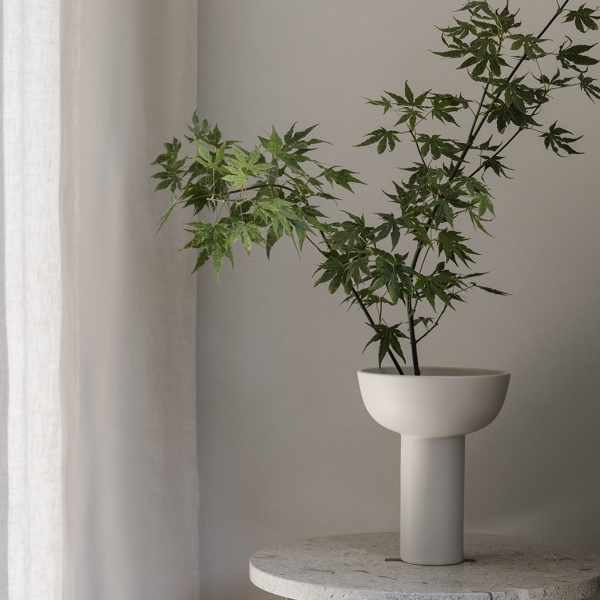 Elegante Vase mit grünen Ästen vor einem sanften, neutralen Hintergrund.