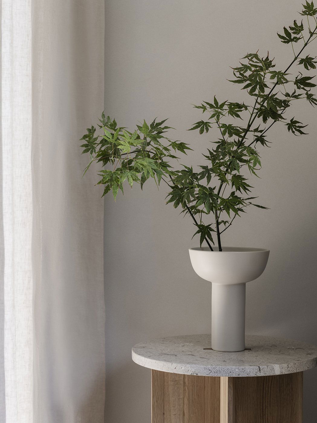 Elegante Vase mit grünen Ästen vor einem sanften, neutralen Hintergrund.