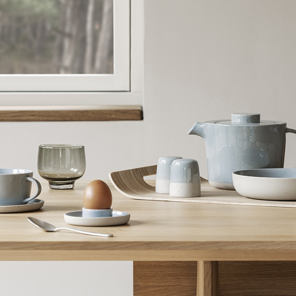 Modern dining table setting with minimalist dishware, including a teapot and egg cup.