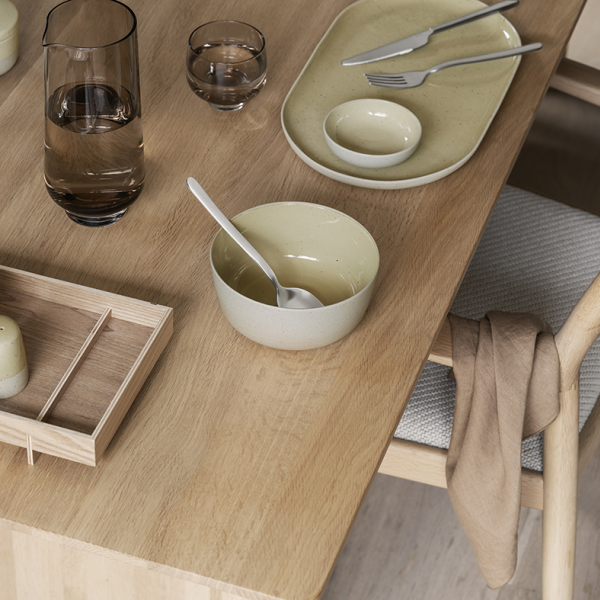 Minimalist dining setup with tableware on a wooden table, featuring bowls and glassware.