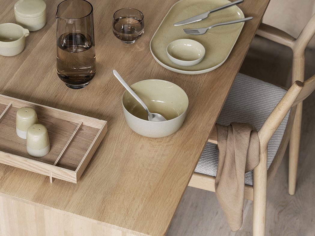 Minimalist dining setup with tableware on a wooden table, featuring bowls and glassware.