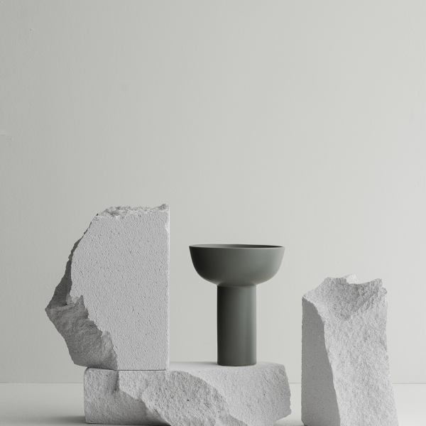 Minimalistische Vase auf strukturiertem Steindisplay vor einem hellen Hintergrund.