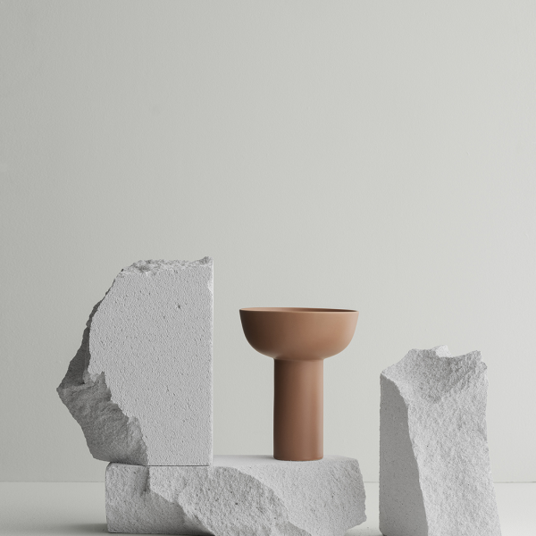 Modernes Keramikgefäß, das auf strukturierten weißen Steinblöcken vor einem minimalistischen Hintergrund präsentiert wird.