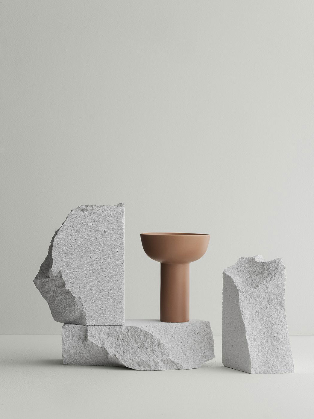 Modernes Keramikgefäß, das auf strukturierten weißen Steinblöcken vor einem minimalistischen Hintergrund präsentiert wird.