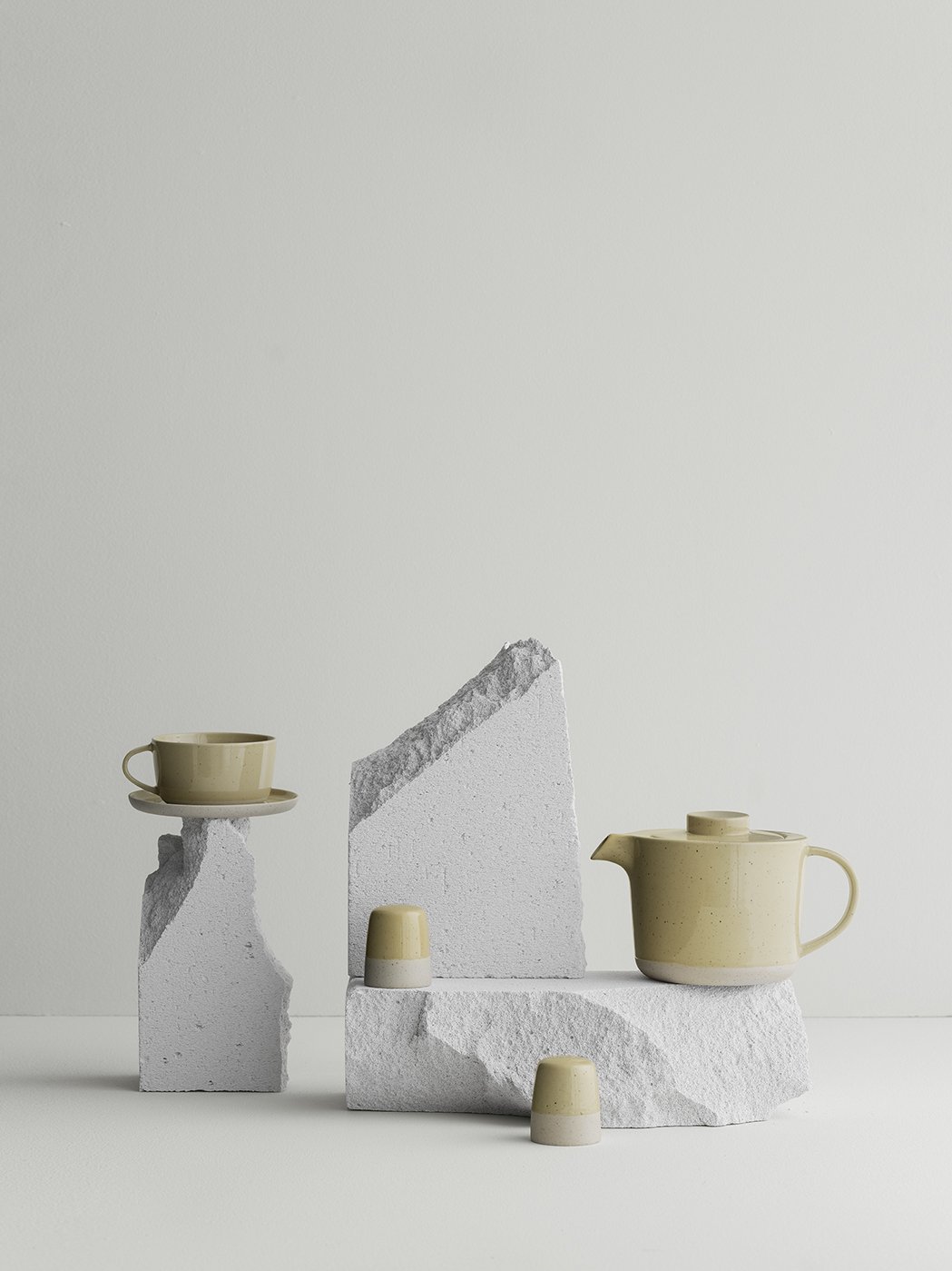 Stylish minimalist tea set displayed on textured stone pedestals against a neutral background.
