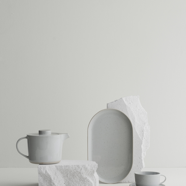 Elegantes weißes Teeset mit strukturierten Steinelementen vor einem minimalistischen Hintergrund.