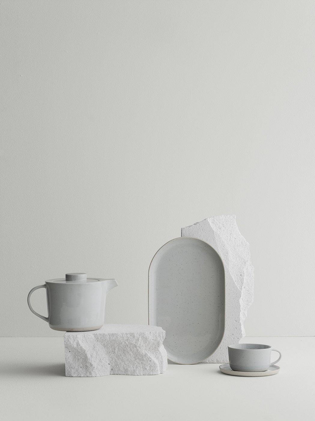 Elegantes weißes Teeset mit strukturierten Steinelementen vor einem minimalistischen Hintergrund.