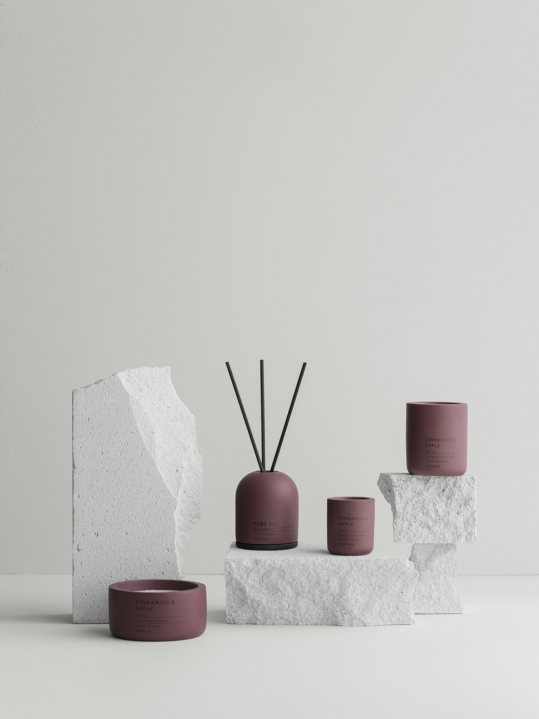 Stylish home fragrance display with diffusers and candles on textured stone pedestal.