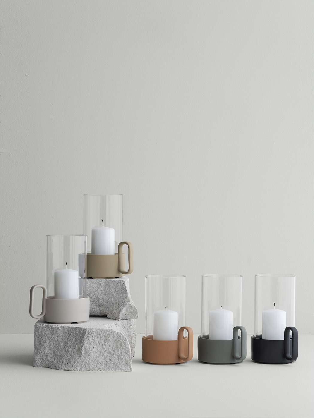 Elegante Glaskerzenhalter mit minimalistischen Designs und neutralen Farben auf einem Steinfuss.