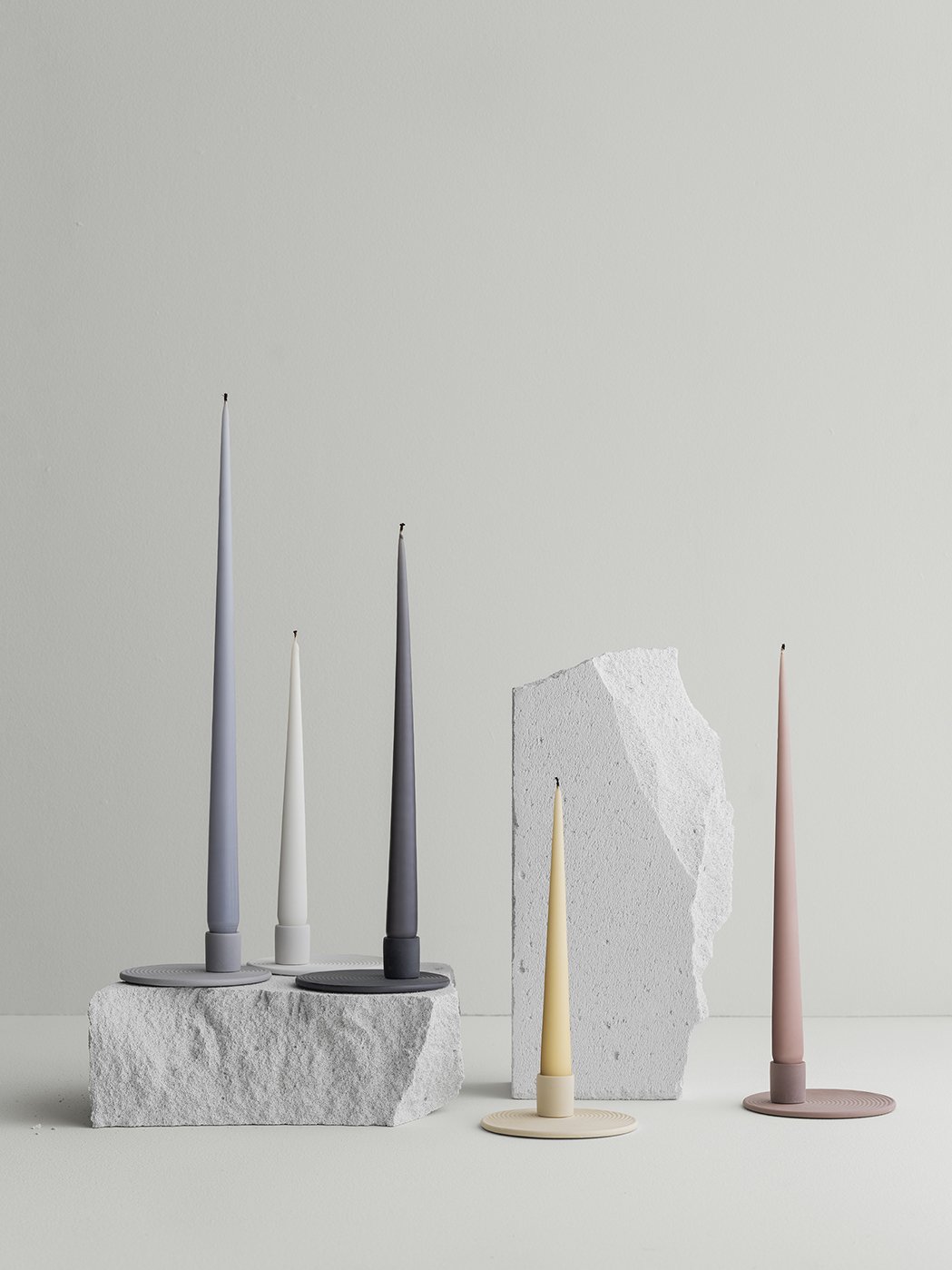 Modern candle holders in minimalist design, featuring various colors and textures on a light backdrop.
