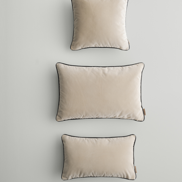 Drei elegante beige Kissen mit schwarzem Besatz, die vertikal vor einem hellen Hintergrund angeordnet sind.