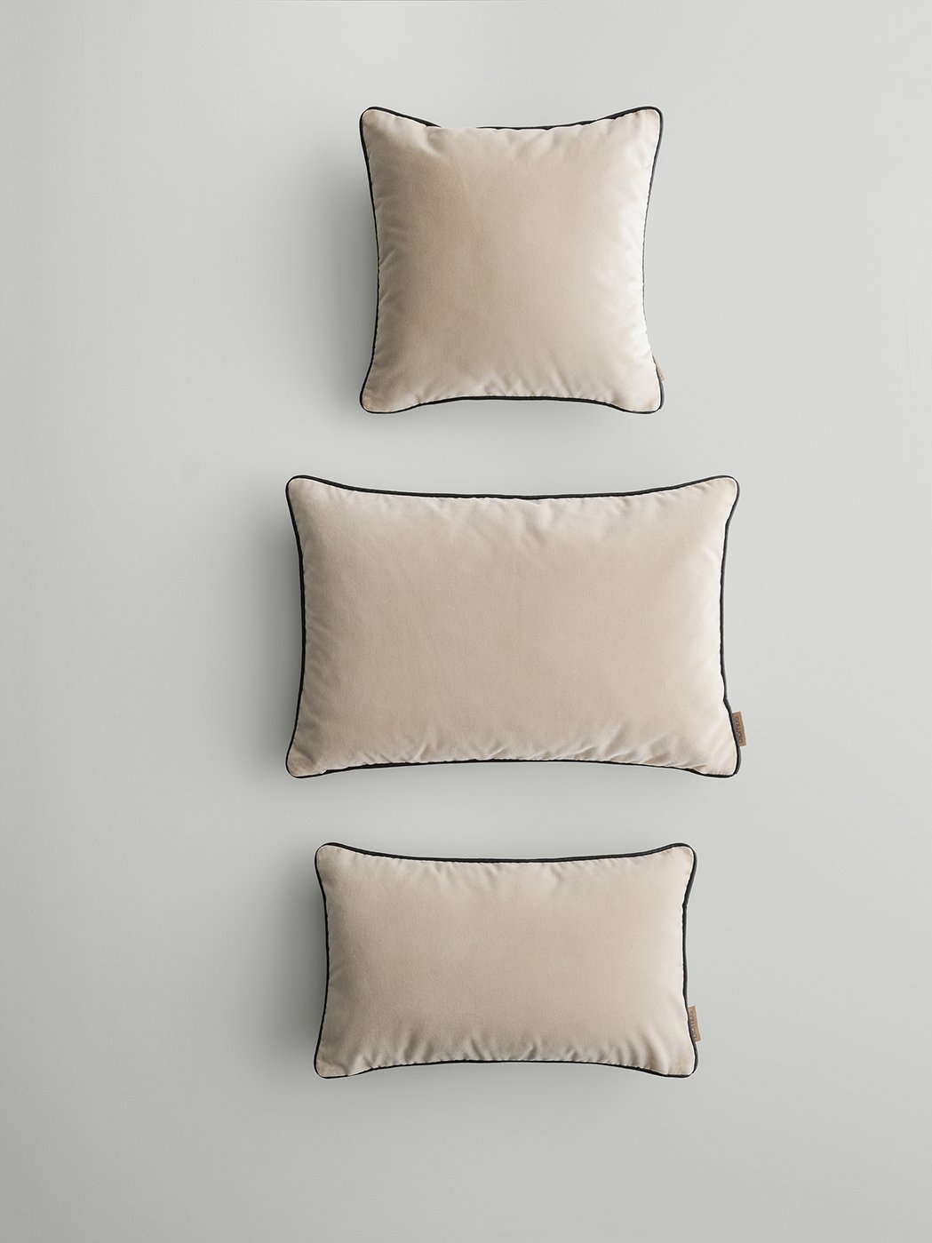 Drei elegante beige Kissen mit schwarzem Besatz, die vertikal vor einem hellen Hintergrund angeordnet sind.