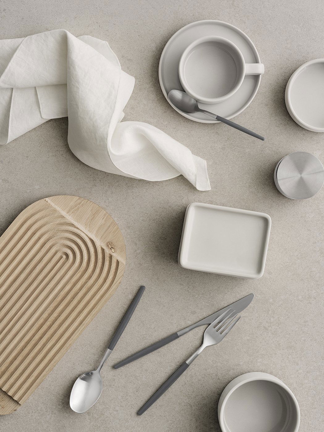 Minimalistische Tischdekoration mit grauem Geschirr und einem Holzserviertablett.
