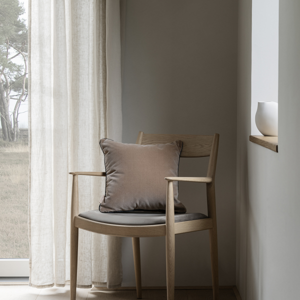 Gemütlicher Holzstuhl mit einem weichen Kissen in einem ruhigen, minimalistischen Innenraum.