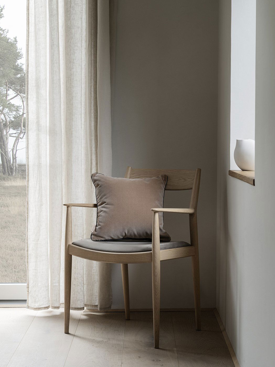 Gemütlicher Holzstuhl mit einem weichen Kissen in einem ruhigen, minimalistischen Innenraum.