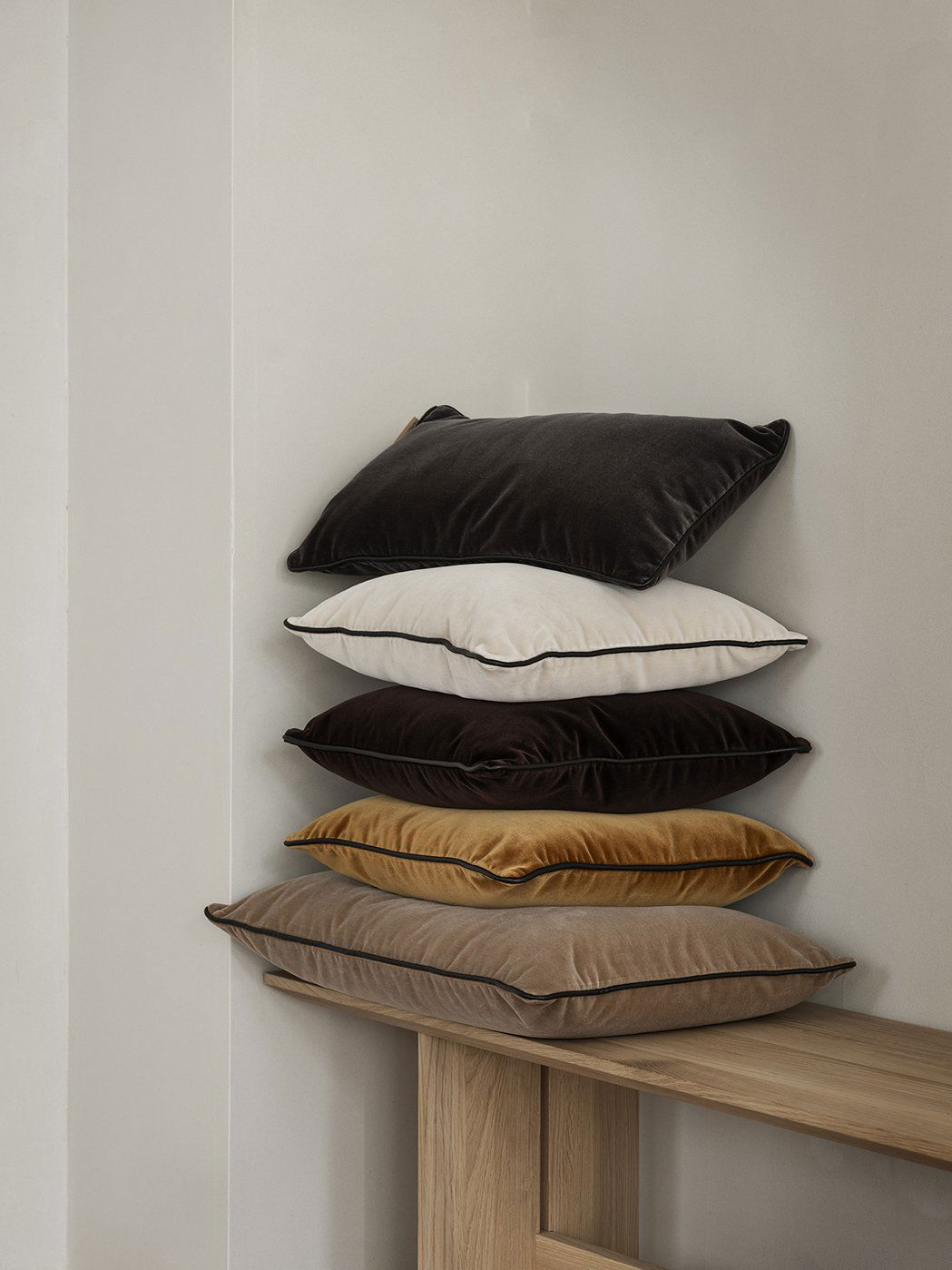 Stack of luxurious velvet throw pillows in various colors displayed on a wooden shelf.
