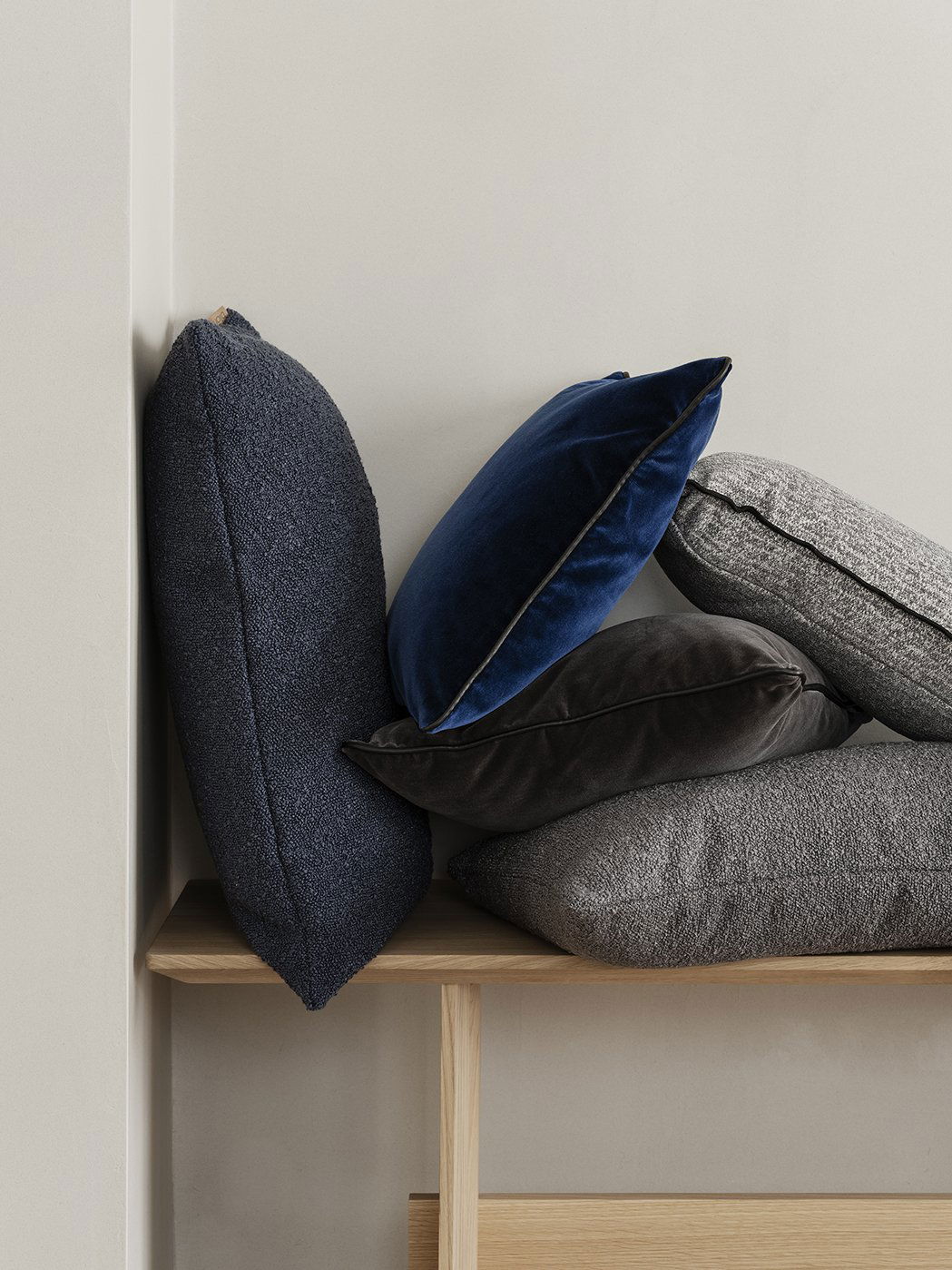 Stacked decorative pillows in various textures and colors on a wooden shelf.