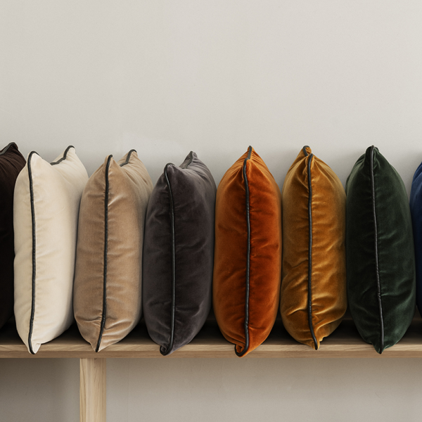 Stylish velvet pillows in various colors neatly arranged on a wooden shelf.