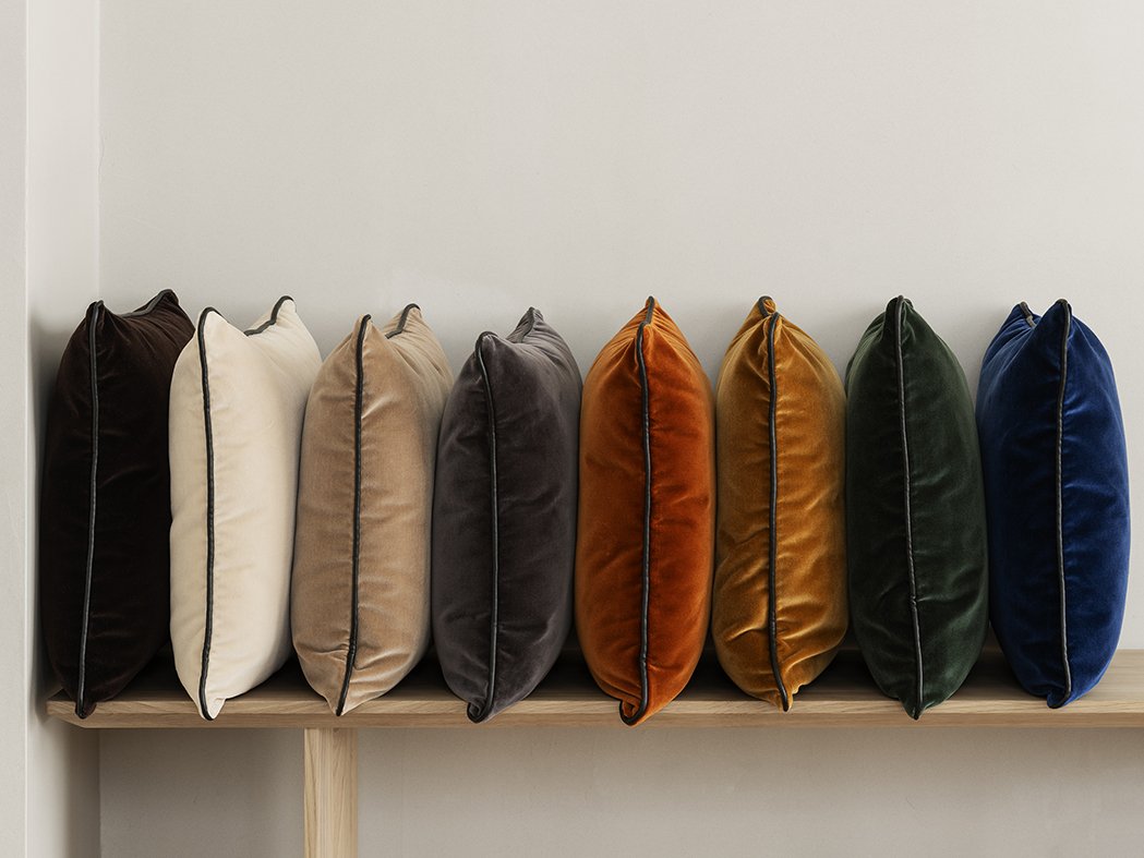 Stylish velvet pillows in various colors neatly arranged on a wooden shelf.