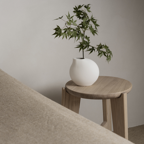 Minimalistische Dekoration mit einer weißen Vase und einer Pflanze auf einem Holzschemel.