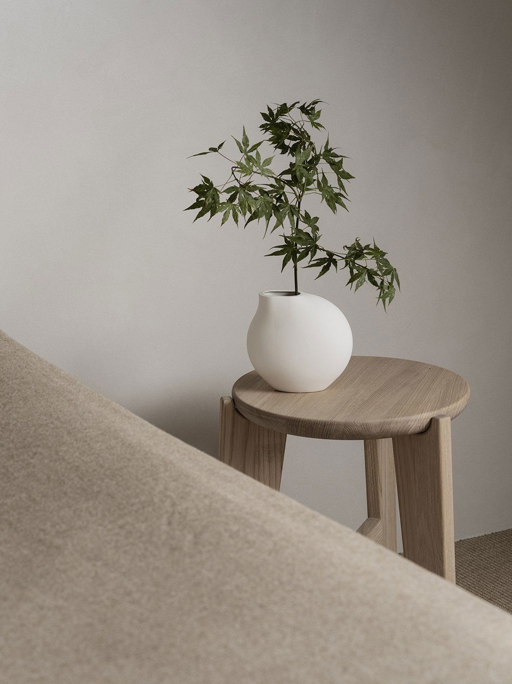 Minimalistische Dekoration mit einer weißen Vase und einer Pflanze auf einem Holzschemel.